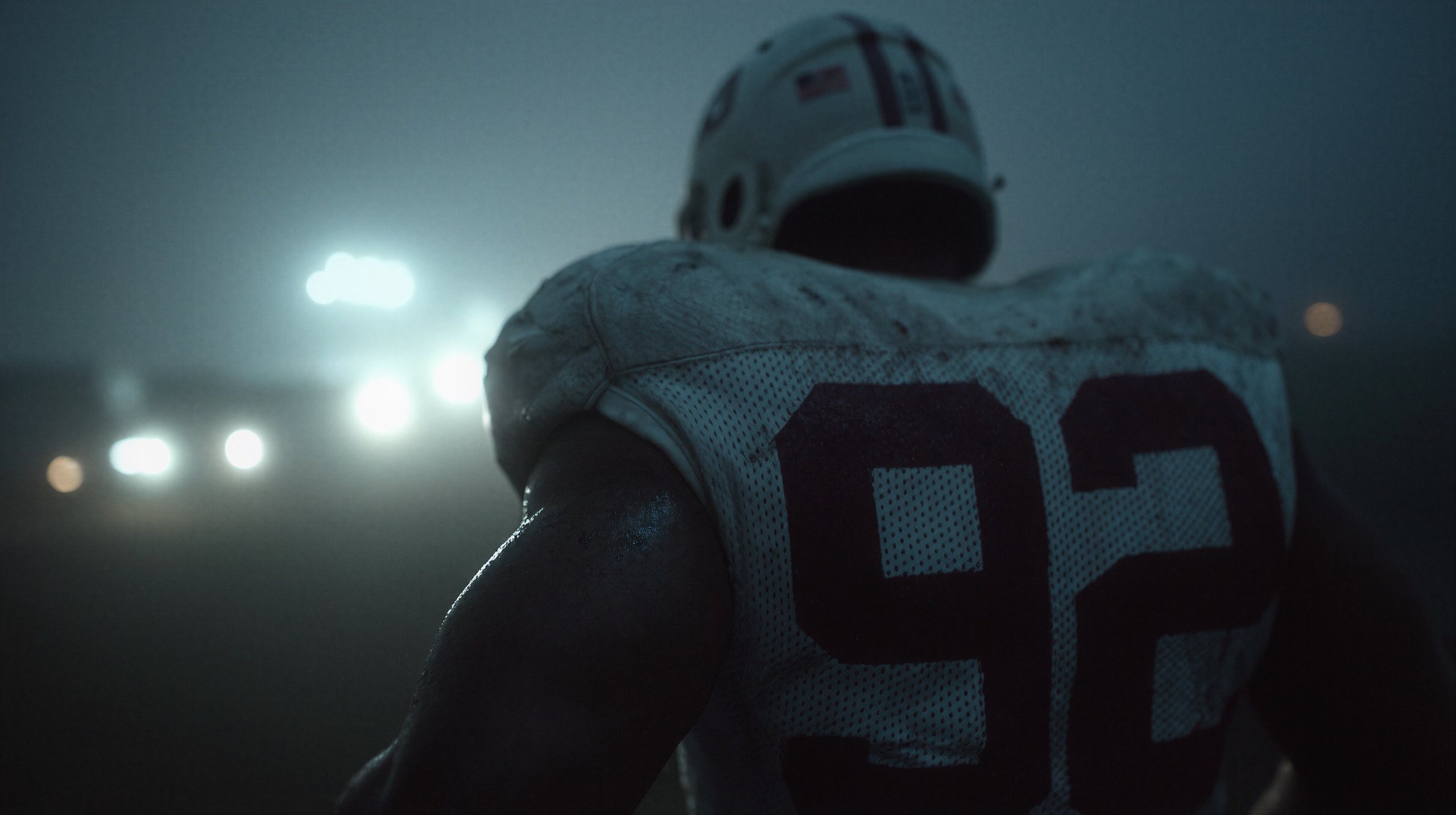 American football player seen from behind, facing stadium floodlights in the fog
